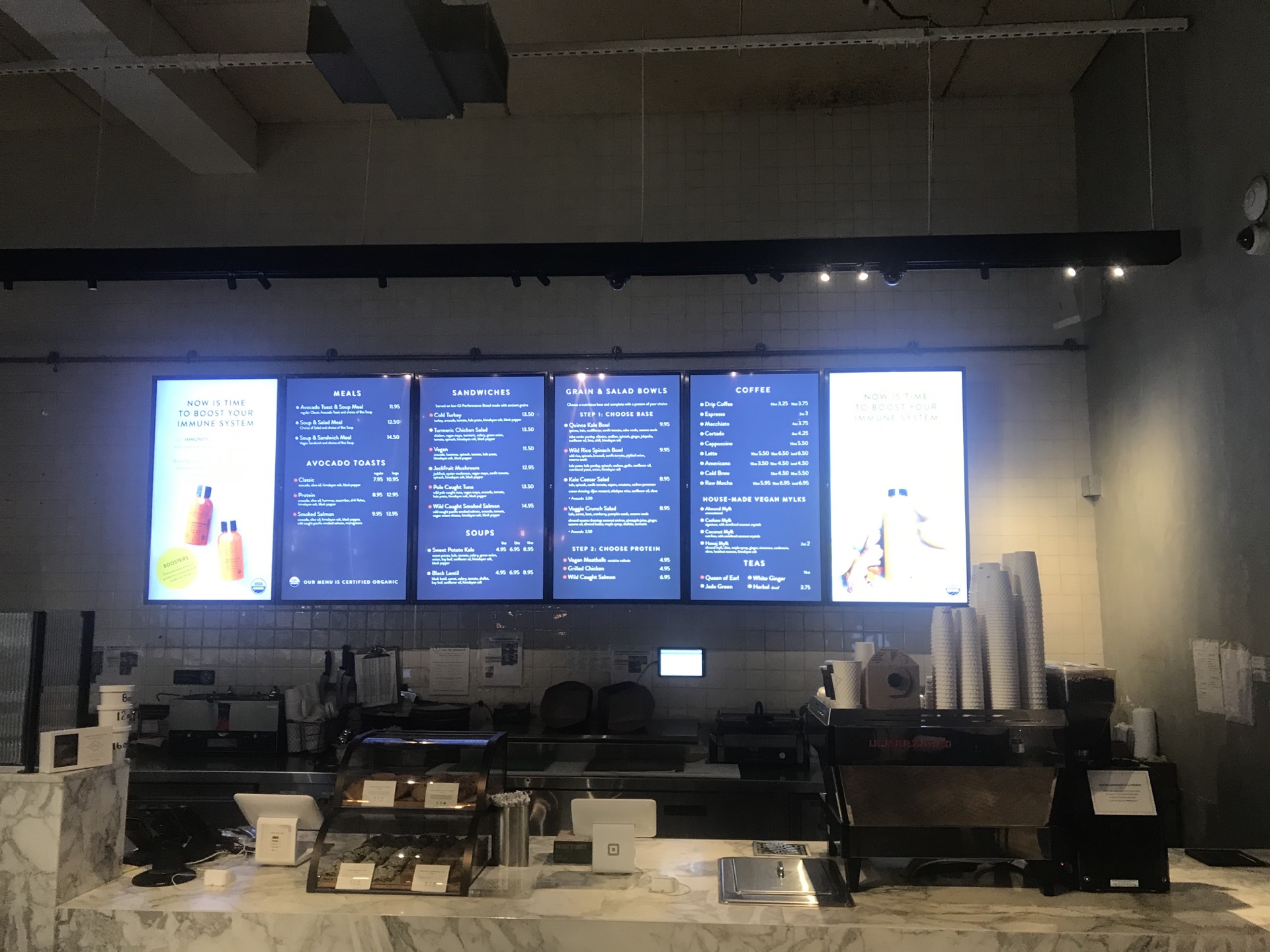 Six vertical digital menu boards above a cafe counter